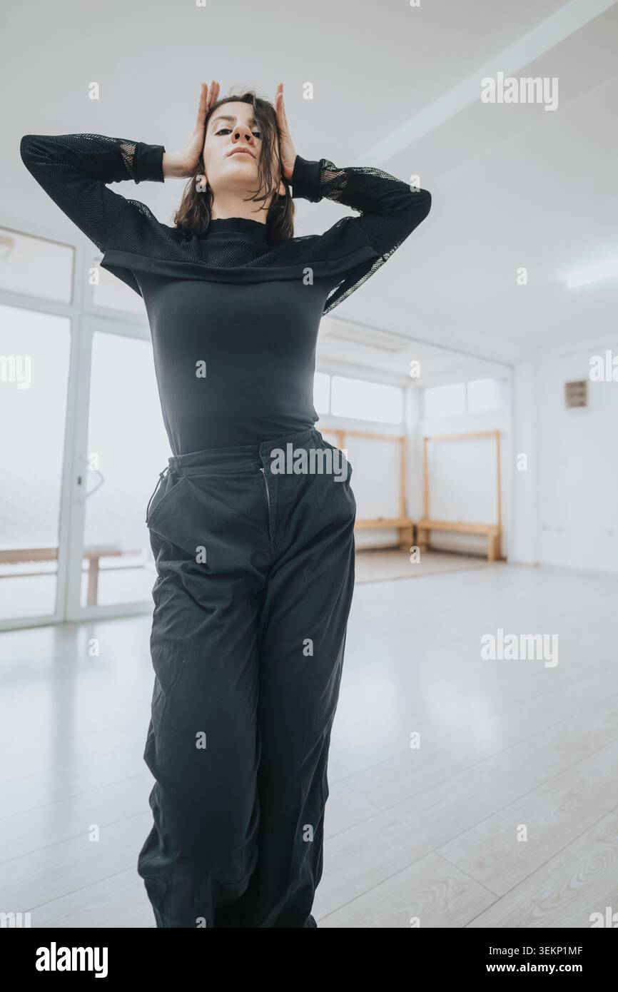 Young female dancer striking a contemporary pose in a bright modern dance studio during rehearsal Stock Photo