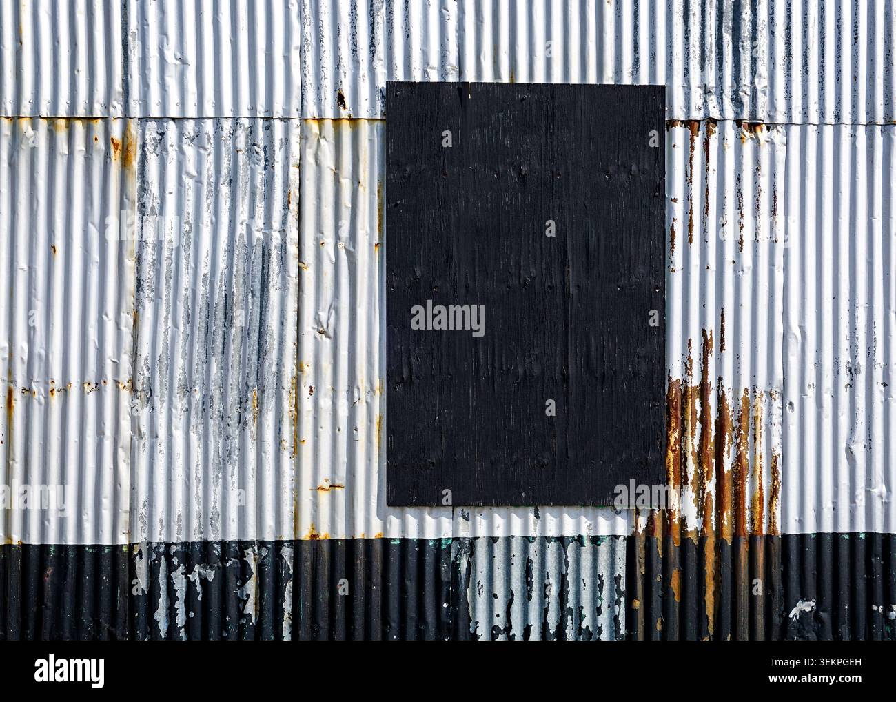 Corroding corrugated metal wall featuring a boarded-up black rectangle creating an abstract pattern Stock Photo