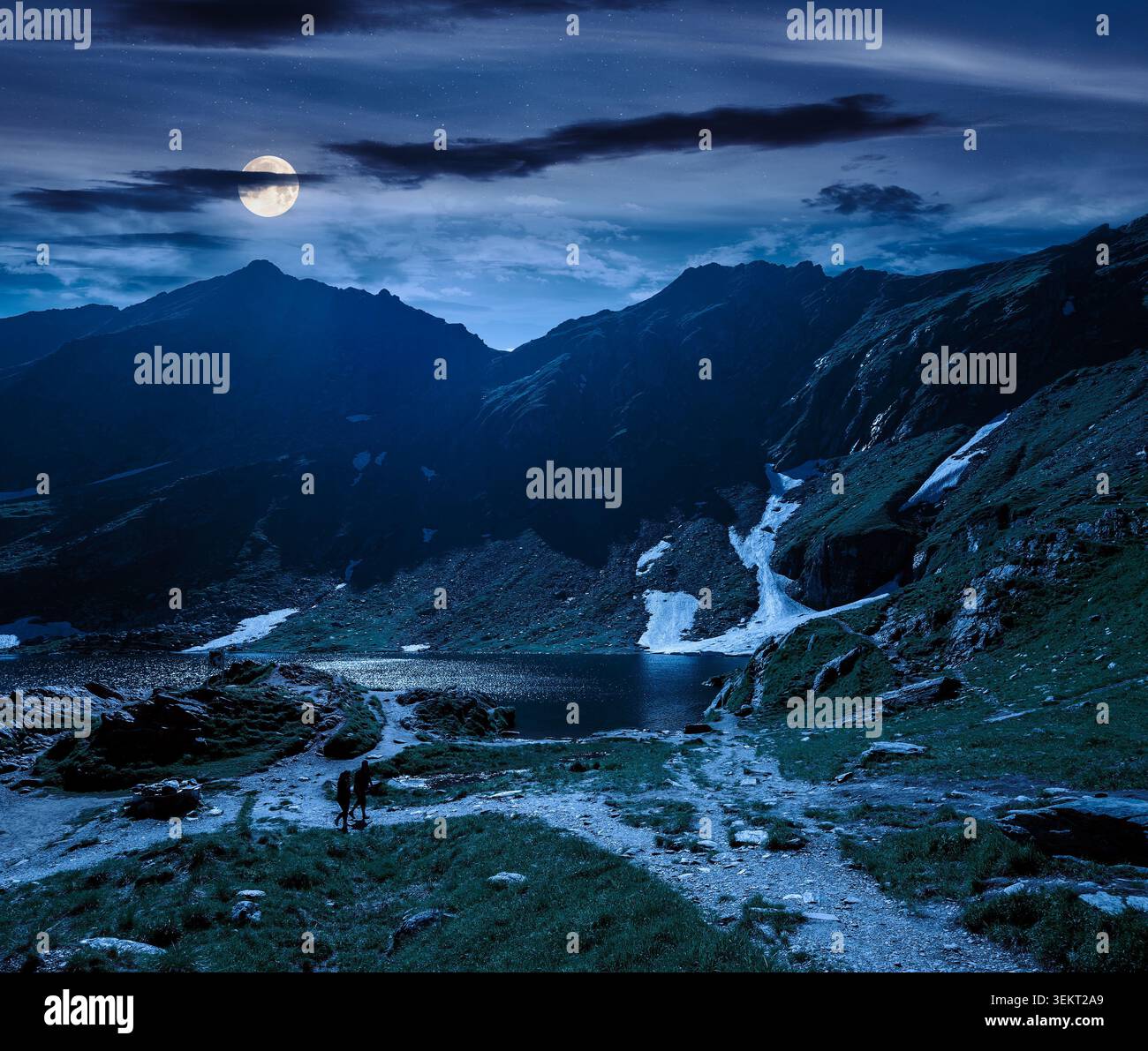 beautiful alpine scenery of fagaras mountains at night. full moon over lake in romania mountain landscape. summer weather with dark sky. rippled water Stock Photo