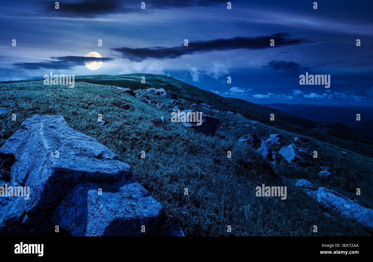 Carpathian mountain summer landscape at night. full moon over meadow with huge stones among the grass on top of the hillside near the peak of mountain Stock Photo