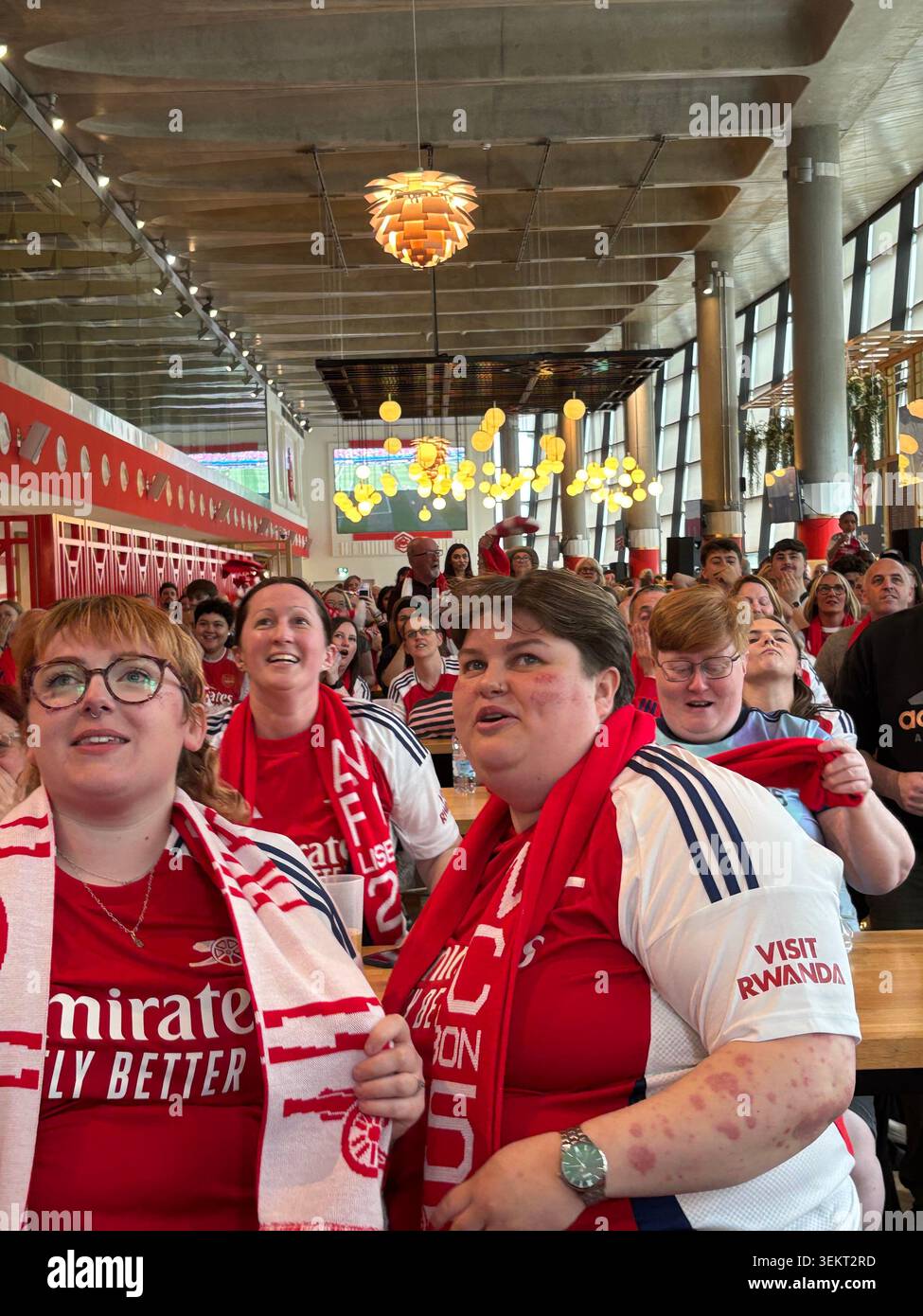 Arsenal Fans watching a live match broadcast together in a crowded indoor sports bar and fan zone venue - Smartphone Captured Stock Image