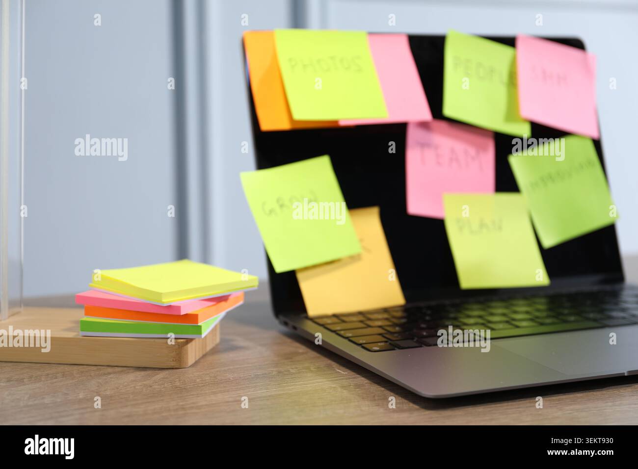 Computer with colorful sticky notes on wooden table, selective focus. Multitasking, deadline and rush at work Stock Photo