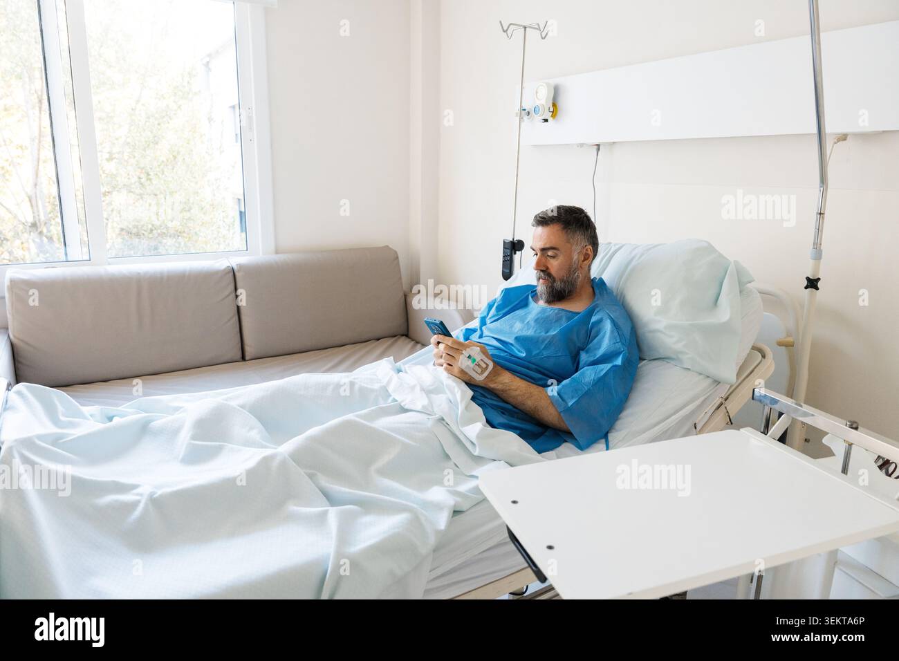 Male patient using smartphone recovering in hospital bed Stock Photo