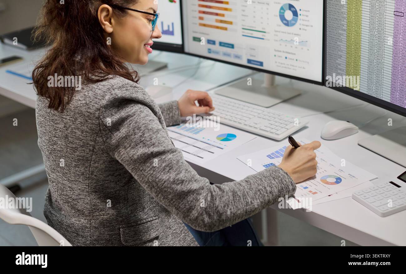 Female accountant analyzing financial data on computer monitors with spreadsheets Stock Photo