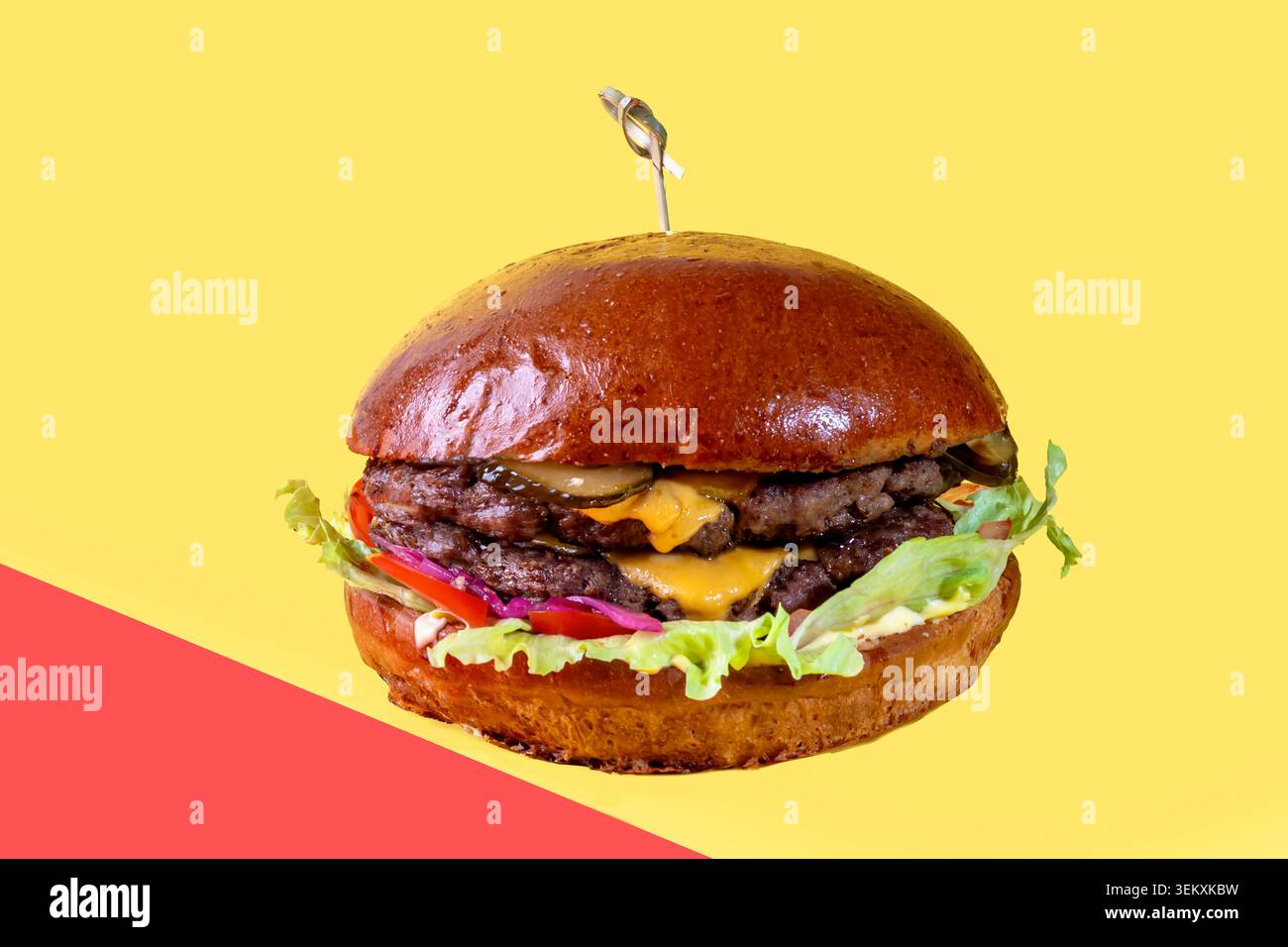 Delicious burger on the board with cutlet, tomatoes and cheese, cucumber and lettuce. On a red background. Fast food. Stock Photo