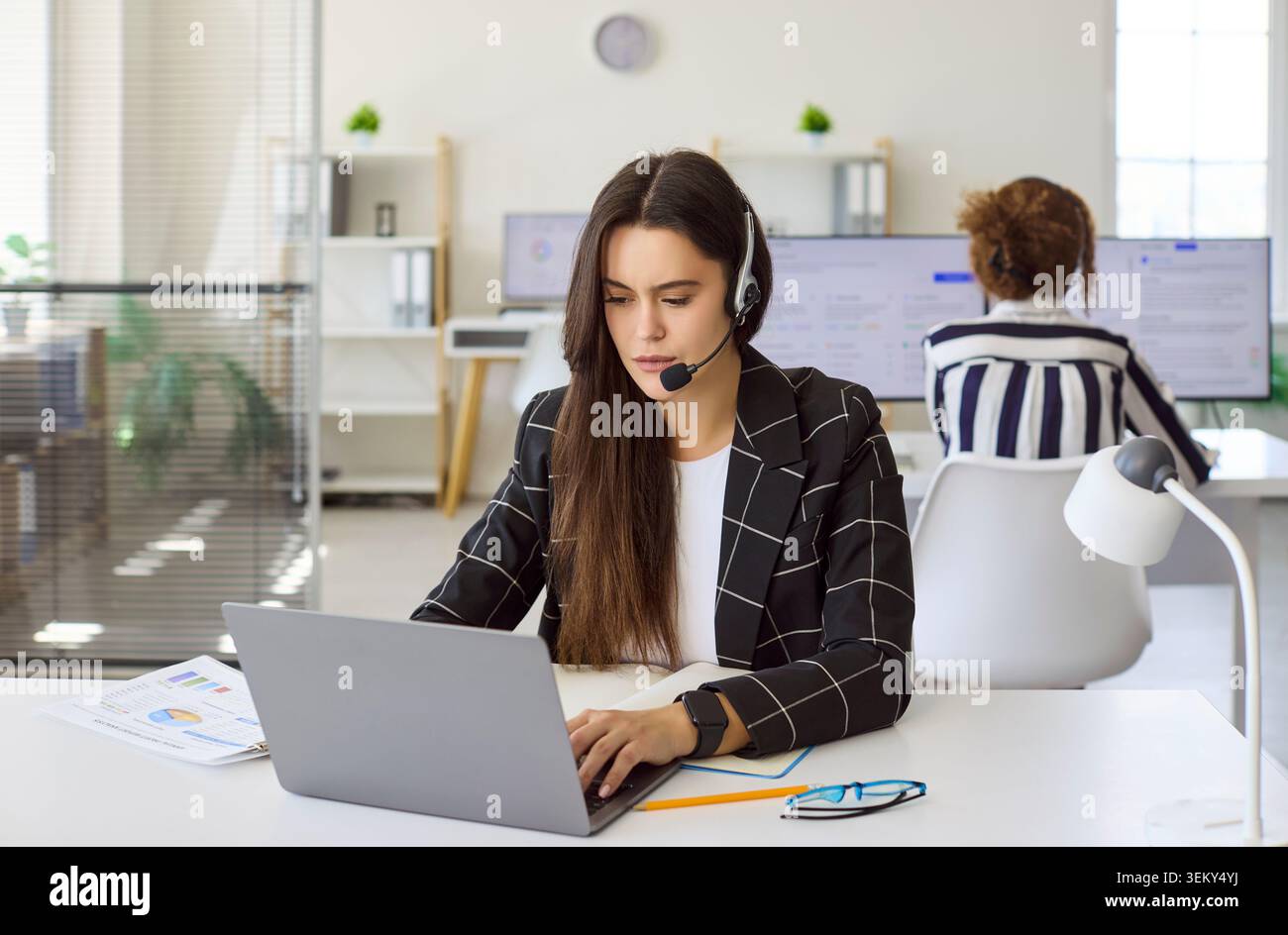 Young woman customer service operator with headset working at computer in office Stock Photo