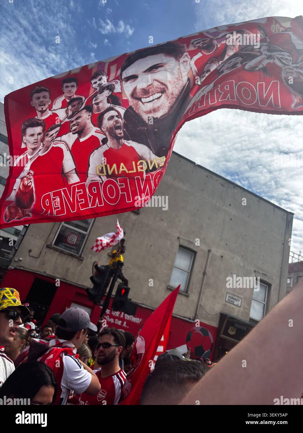 Arsenal supporters celebrating near Emirates Stadium in North London, with a red Arsenal flag waved above the crowd. - Smartphone Captured Stock Image