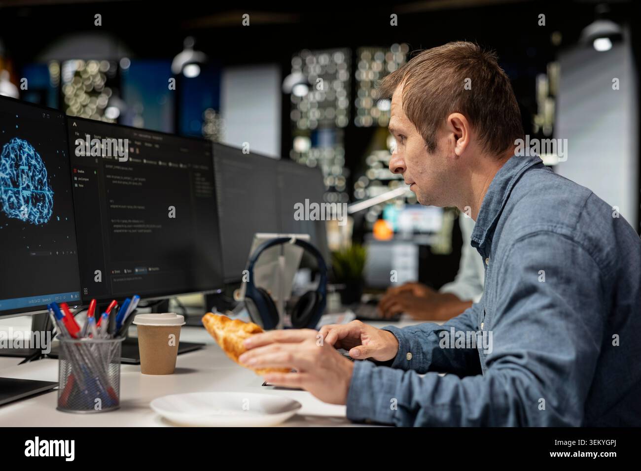 Admin eating croissant while using computer in tech startup office to develop programs with AI. IT professional enjoying snack break while debugging applications with artificial intelligence Stock Photo