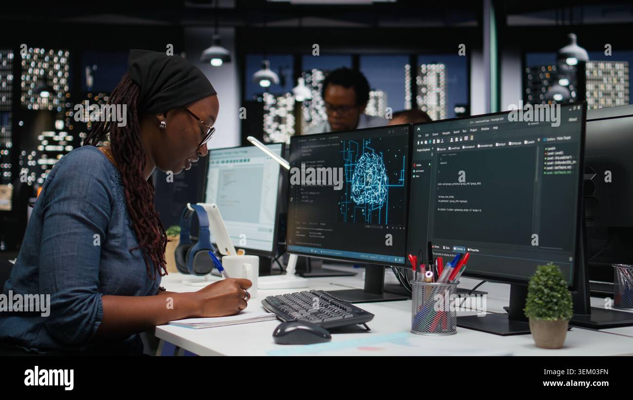 Software developer in office writing on notepad, working to fix bugs in artificial intelligence system. IT expert taking notes at desk, troubleshooting neural network errors in tech startup Stock Photo