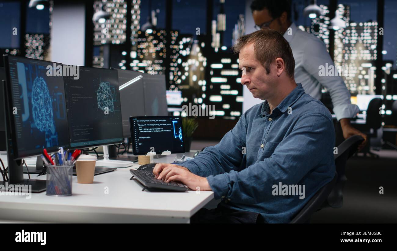 Tech startup IT expert developing artificial intelligence algorithms in high rise office late at night. System administrator debugging neural network brain models on screens Stock Photo