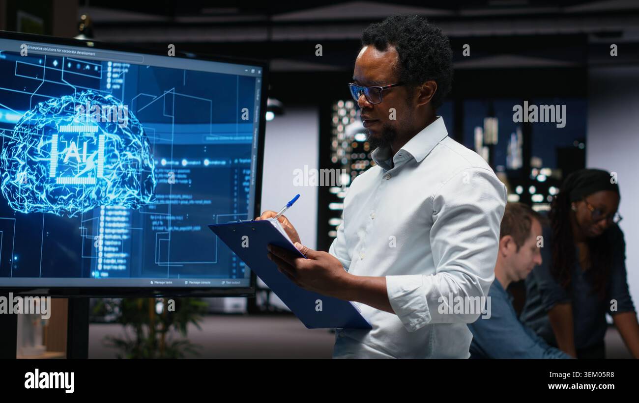 Manager in office writing on notepad, taking notes of artificial intelligence system bugs to fix. Supervisor looking at large screen, documenting neural network errors during troubleshooting Stock Photo