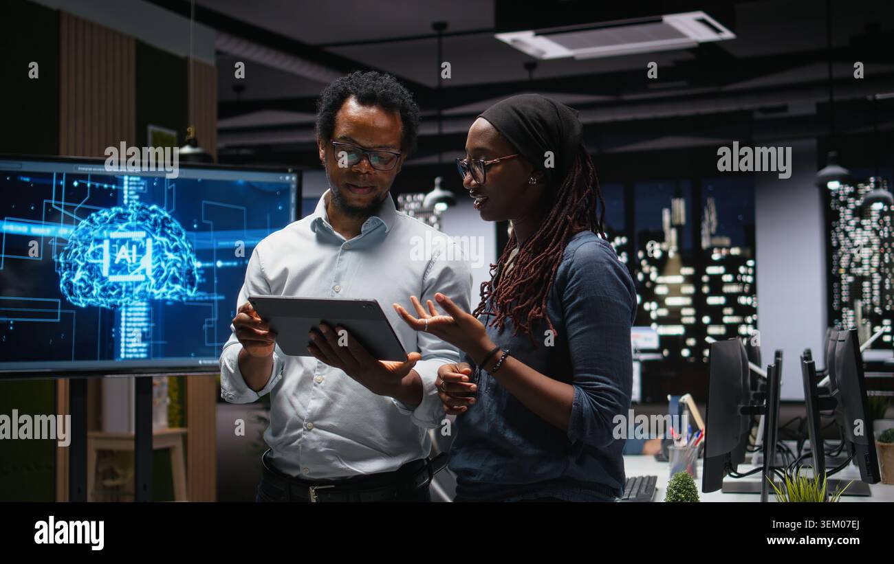Tech agency staff members using tablet, brainstorming how to optimize AI performance in office. African american technicians use machine learning on device for debugging, analyzing code Stock Photo