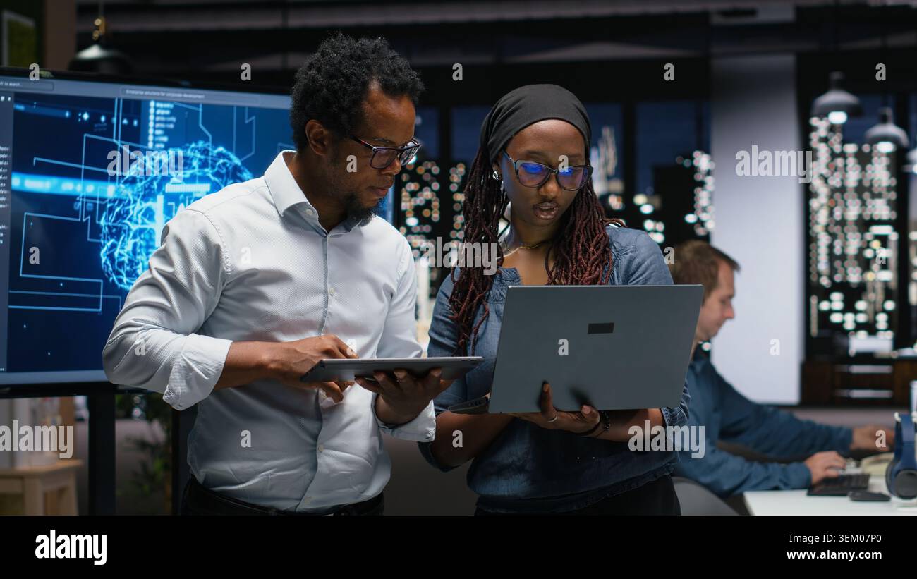Tech agency colleagues collaborating to optimize AI performance in office late at night. Software developers use machine learning on devices for debugging, analyzing code Stock Photo