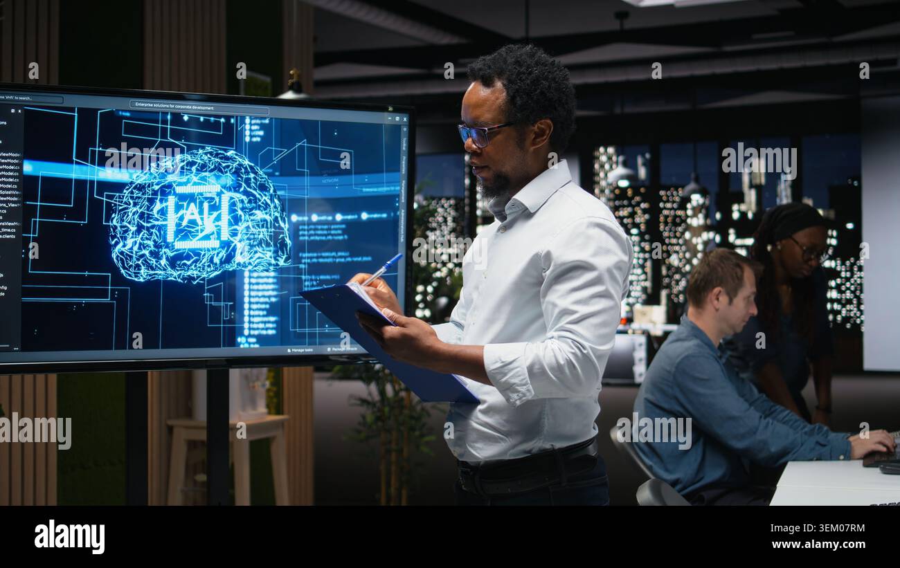 Manager in office writing on notepad, taking notes of artificial intelligence system bugs to fix. Supervisor looking at large screen, documenting neural network errors during troubleshooting Stock Photo