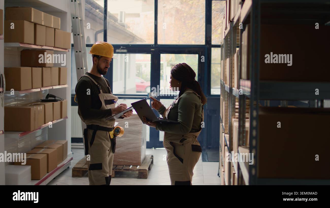 Warehouse chief supply chain officers inputing updated products info on online shopping website, walking through storeroom aisles inspecting labels on wares, crosschecking with inventory list Stock Photo
