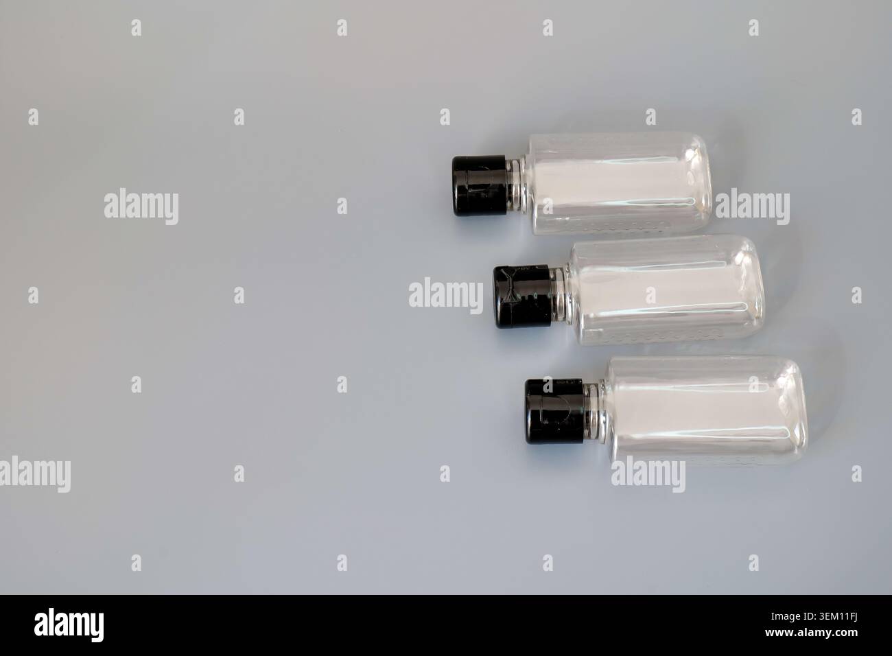 Three clear plastic bottles with black caps on a gray background Stock Photo