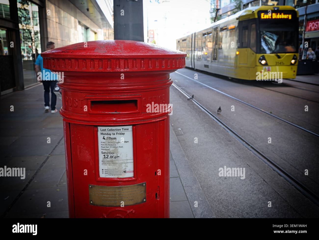 Manchester’s famous red postbox on Corporation Street, which survived the 1996 IRA bombing almost unscathed, beside a passing Metrolink tram. Stock Photo