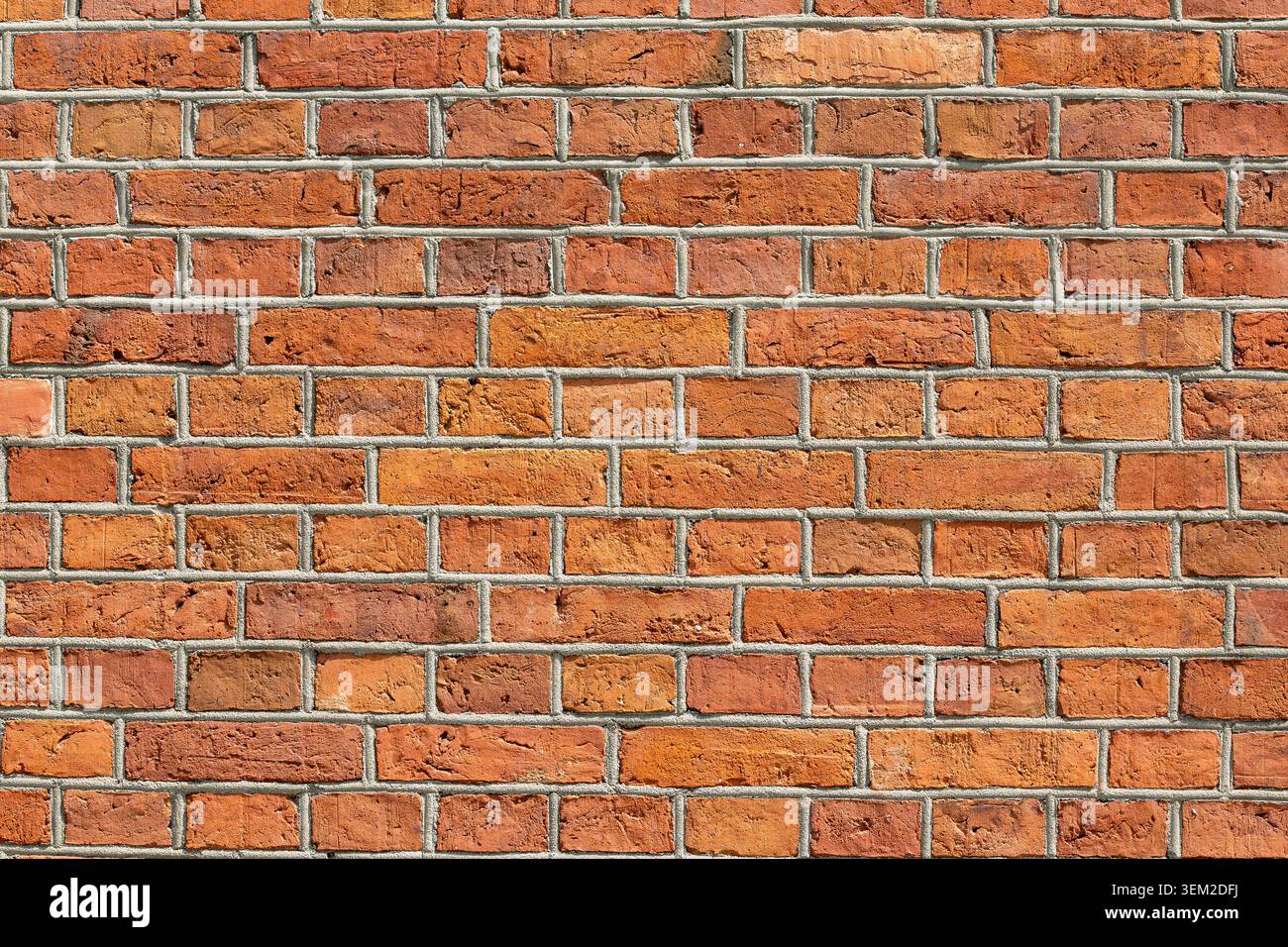 Red brick wall with a weathered surface, gray mortar joints and irregular color variations. Rectangular bricks arranged in a staggered pattern Stock Photo