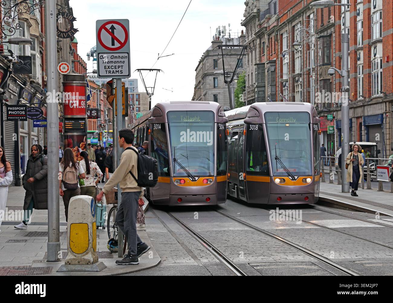 Two Luas Red Line trams pass crowd of pedestrians on busy Abbey Street in Dublin city centre, Ireland, showing integrated light rail. Stock Photo