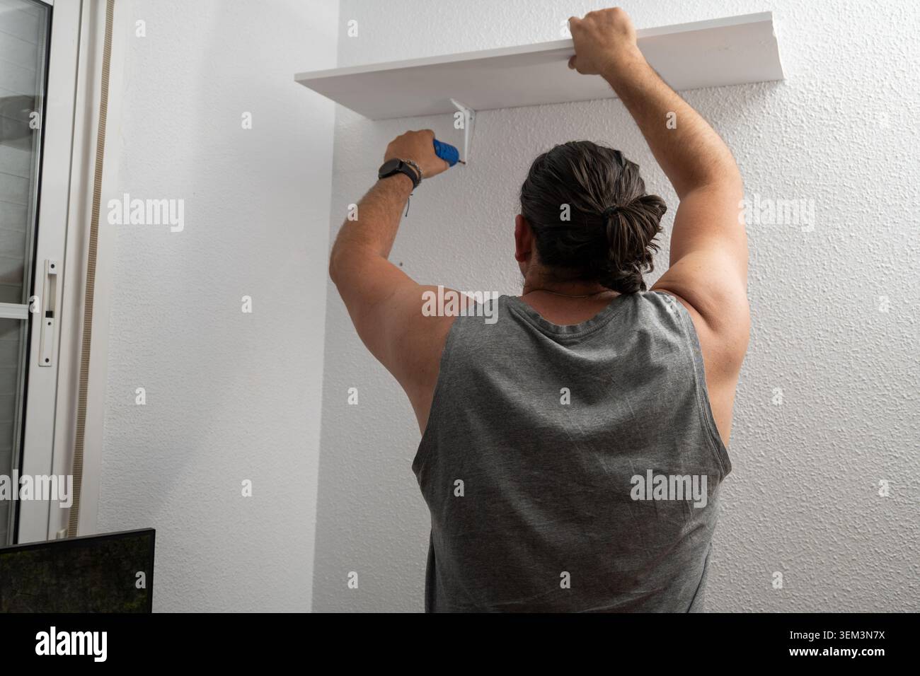Man installing a new shelf with brackets on a white wall Stock Photo