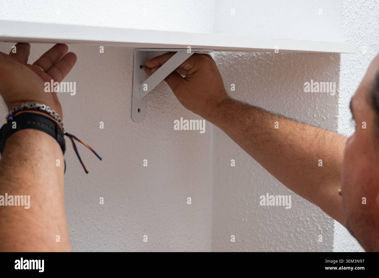 Man installing shelf bracket on wall for home improvement Stock Photo