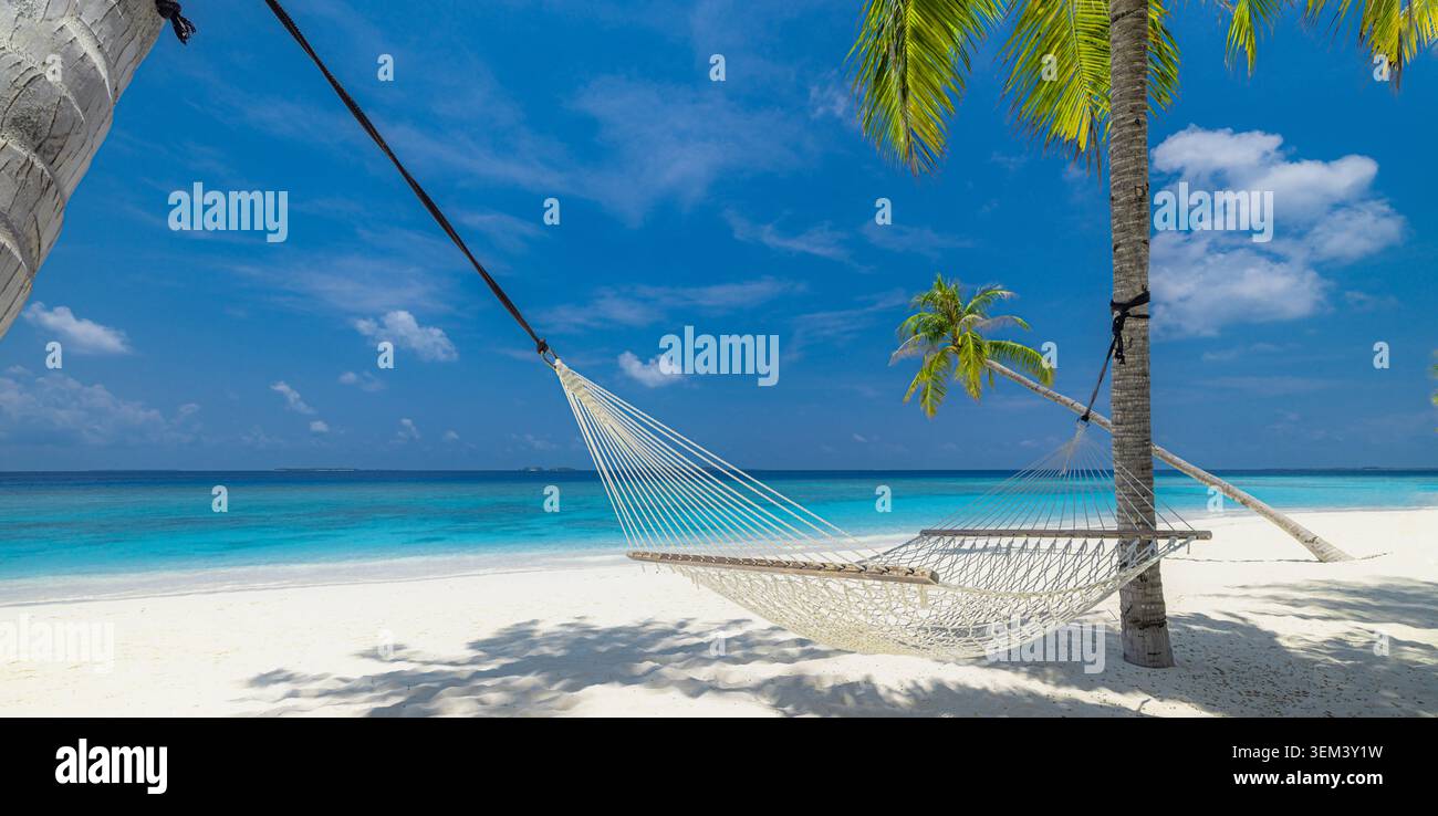 Empty beach hammock swaying between palms above calm turquoise ocean lagoon. Sunny tropical island white sand. Summer holiday travel vacation paradise Stock Photo