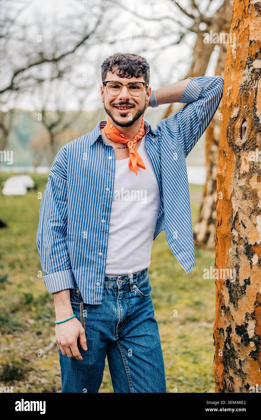 Young man smiling and leaning on tree outdoors Stock Photo