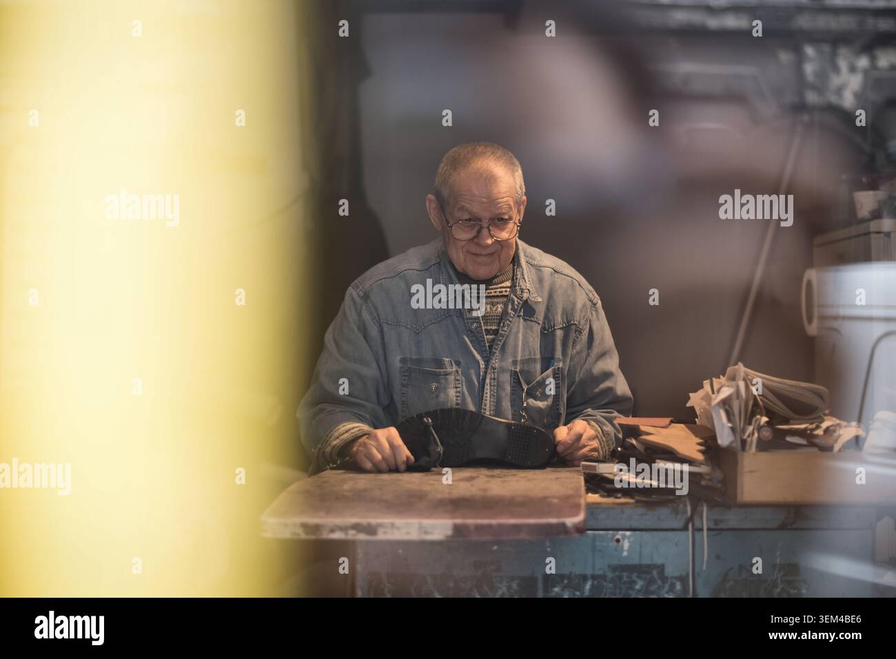 Senior shoemaker smiles while working in workshop Stock Photo