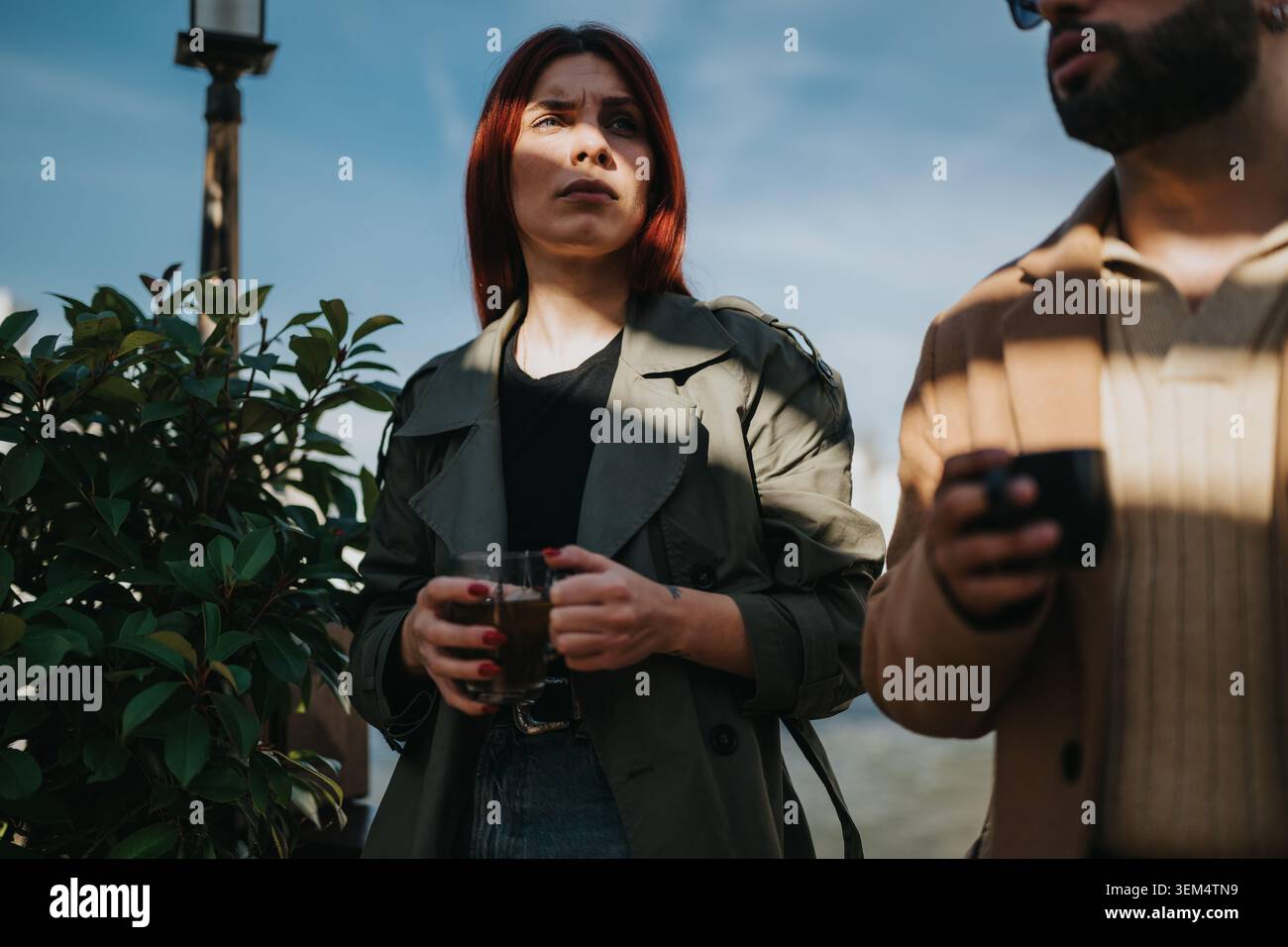 Two colleagues sharing a coffee break outdoors on a sunny urban terrace while talking quietly Stock Photo