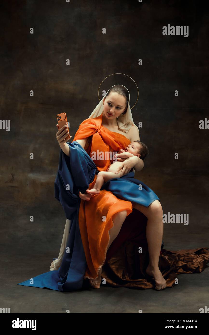 Smiling baroque mother taking selfie while holding baby in studio. Stock Photo