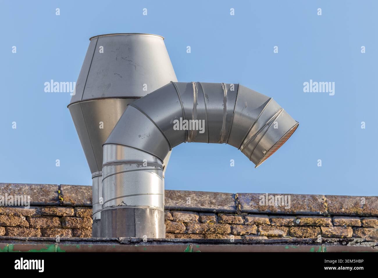 Stainless steel roof-mounted extraction vent used for commercial kitchen ventilation and air handling systems against a clear blue sk Stock Photo