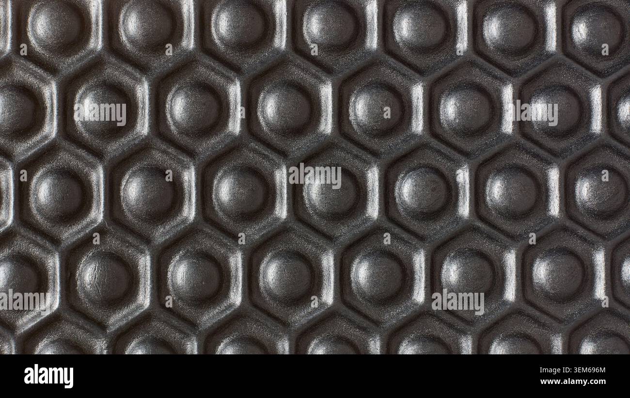 dark black rubber surface with repeating hexagonal honeycomb pattern background texture, raised circular bumps on grip material, full frame macro Stock Photo