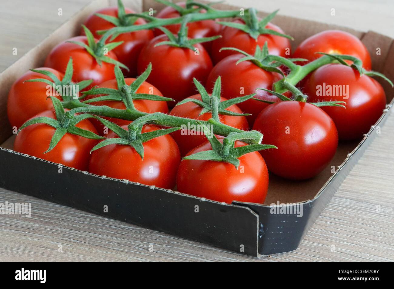 Cherry tomatoes in a cardboard box on a wooden table, top view. Tomatoes from the store. Stock Photo