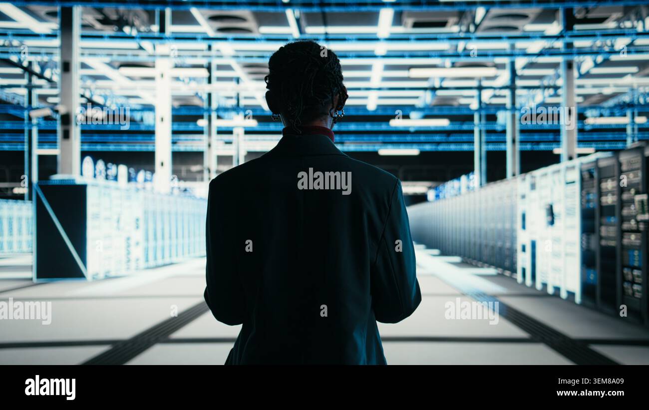Software developer walks in data center, using tablet and AR technology to debug system errors. Server farm IT professional runs diagnostics on blue wireframe mesh equipment supercomputers, camera A Stock Photo