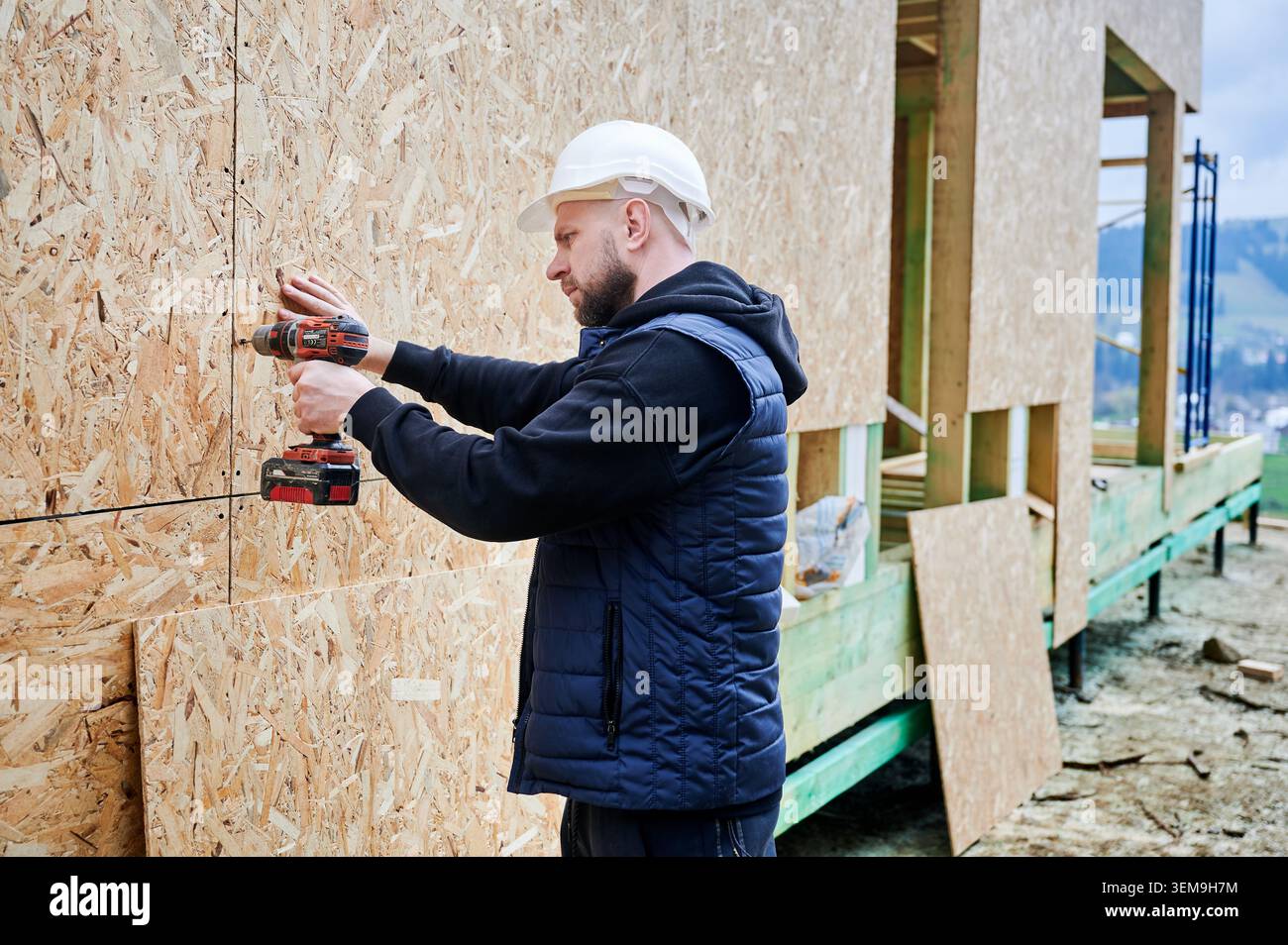 Construction worker fastening sheathing boards to timber structure using power tool, symbolizing home building process, structural development and professional craftsmanship Stock Photo