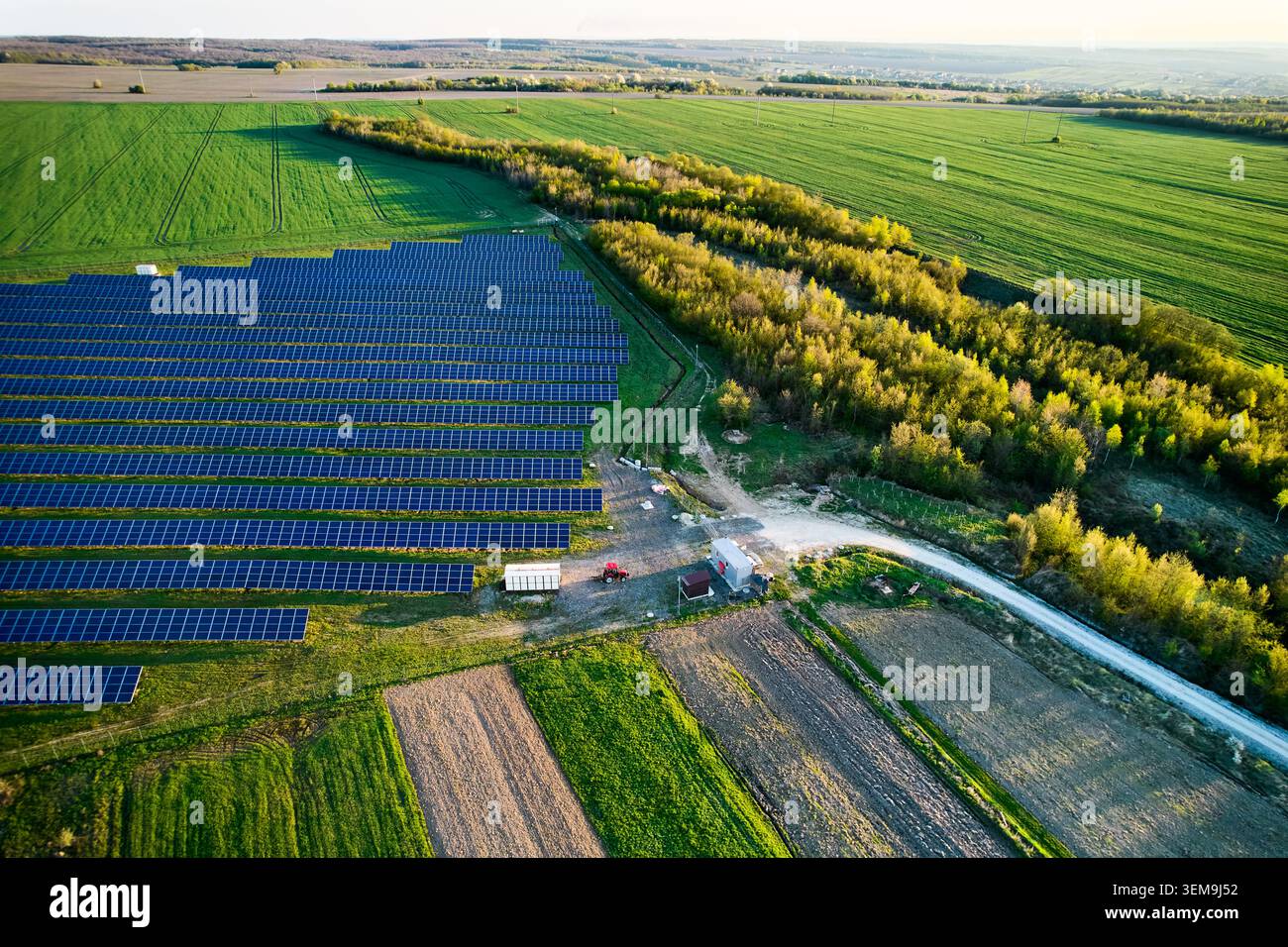 Aerial view of solar farm beside green fields and forest, rows of ...