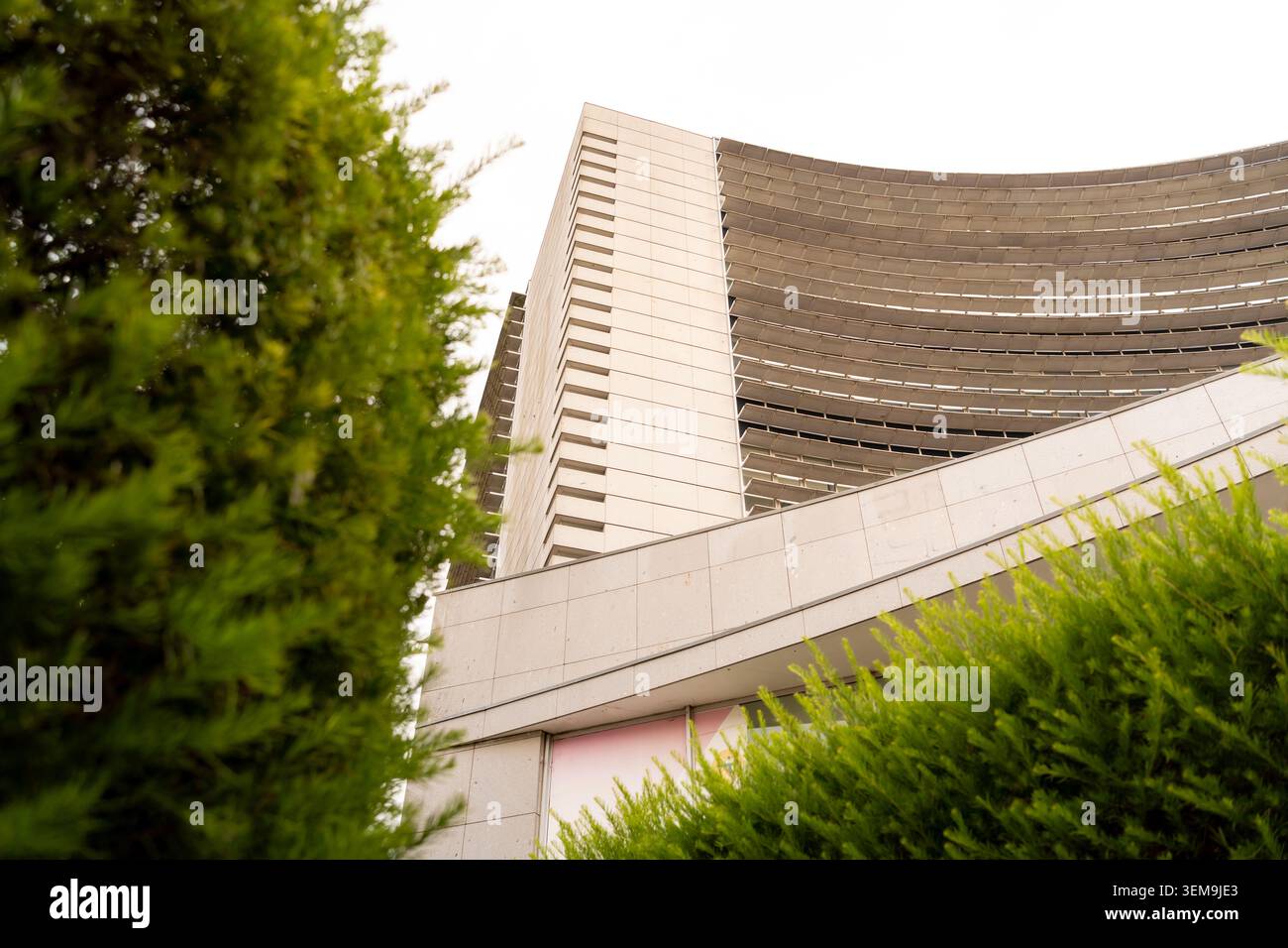 Modern architectural building showcasing curved elements and sharp angles contrasted with green foliage Stock Photo