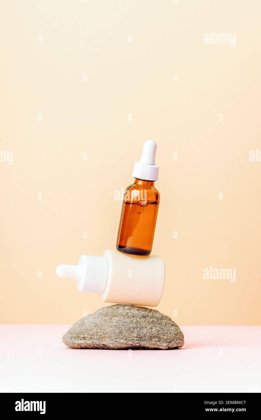 Skincare serum bottles balanced on stone against pastel background with copy space. Stock Photo