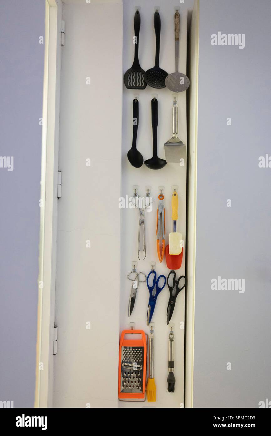 Kitchen utensils hanging on hooks providing efficient storage inside a cabinet door Stock Photo