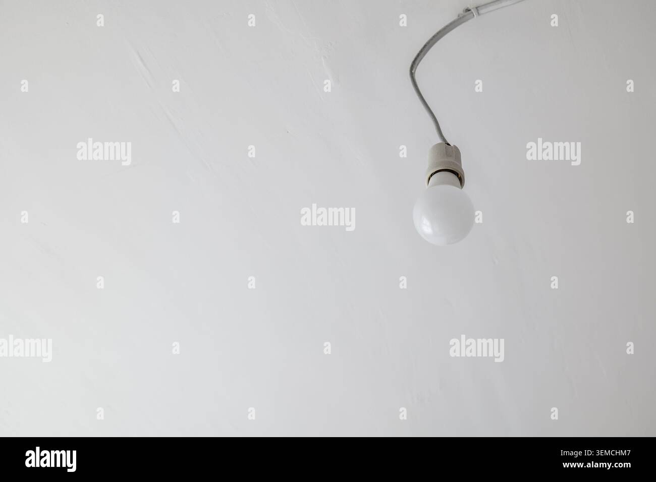 Single light bulb hanging from a wire on a white ceiling Stock Photo