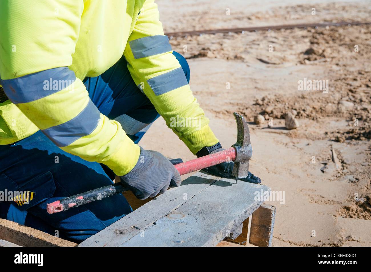 Close-up of a construction worker in high-visibility jacket using a hammer on wooden formwork at an outdoor building site, focused on hands, tools, an Stock Photo
