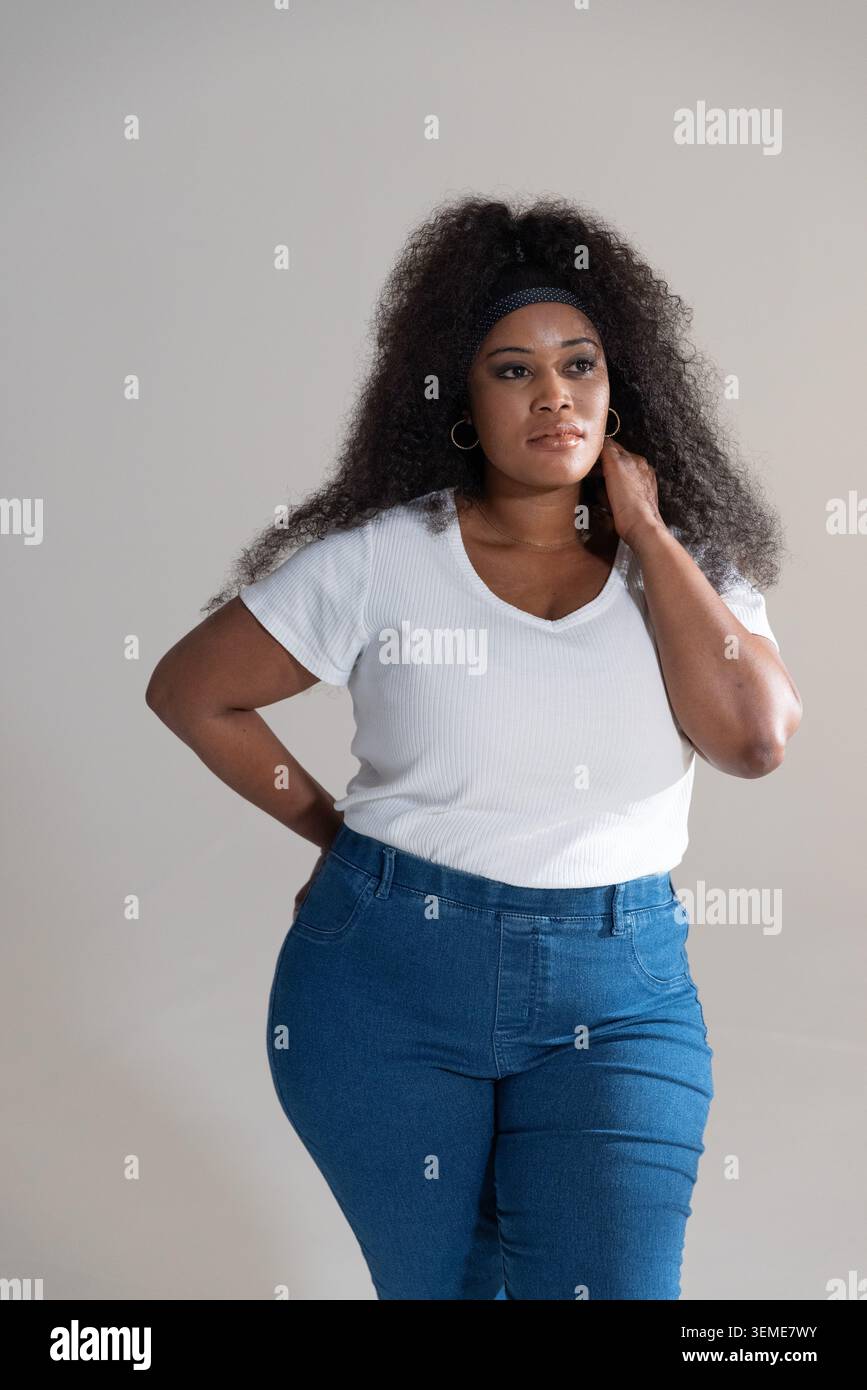 Mid adult African American woman standing in studio wearing white ribbed top and high-waisted jeans Stock Photo