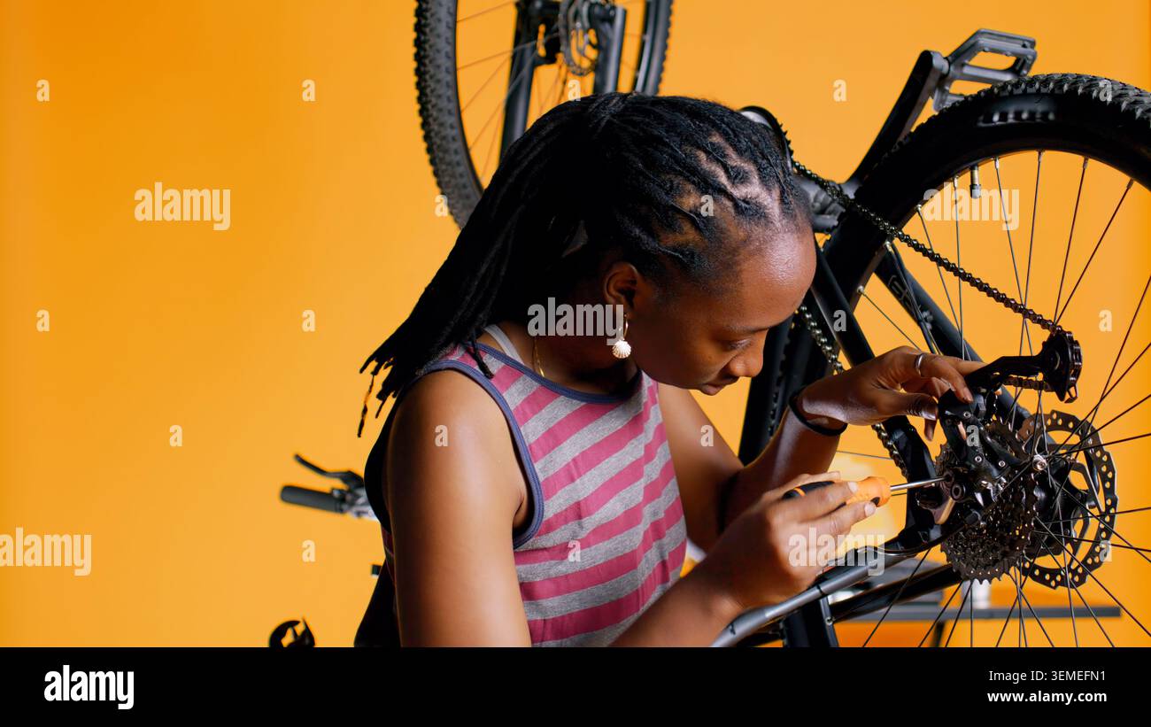Close up of engineer using screwdriver and hex socket wrench to secure wheel on bicycle in studio background. Professional screwing bolts on bike parts, mending rear derailleur and cassette, camera B Stock Photo