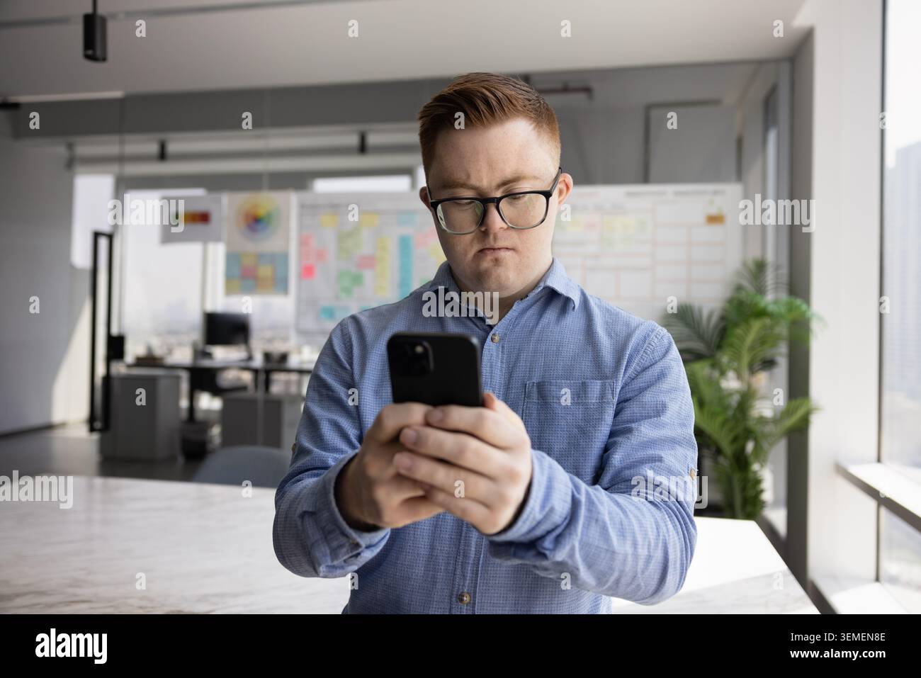 Young man with Down syndrome using mobile phone in office Stock Photo