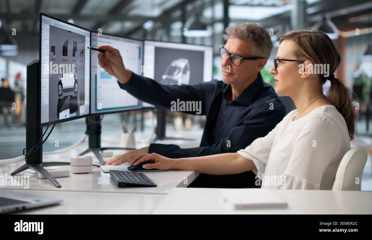 Two Engineers Working On Computer To Develop Car Gearbox Design. Stock Photo
