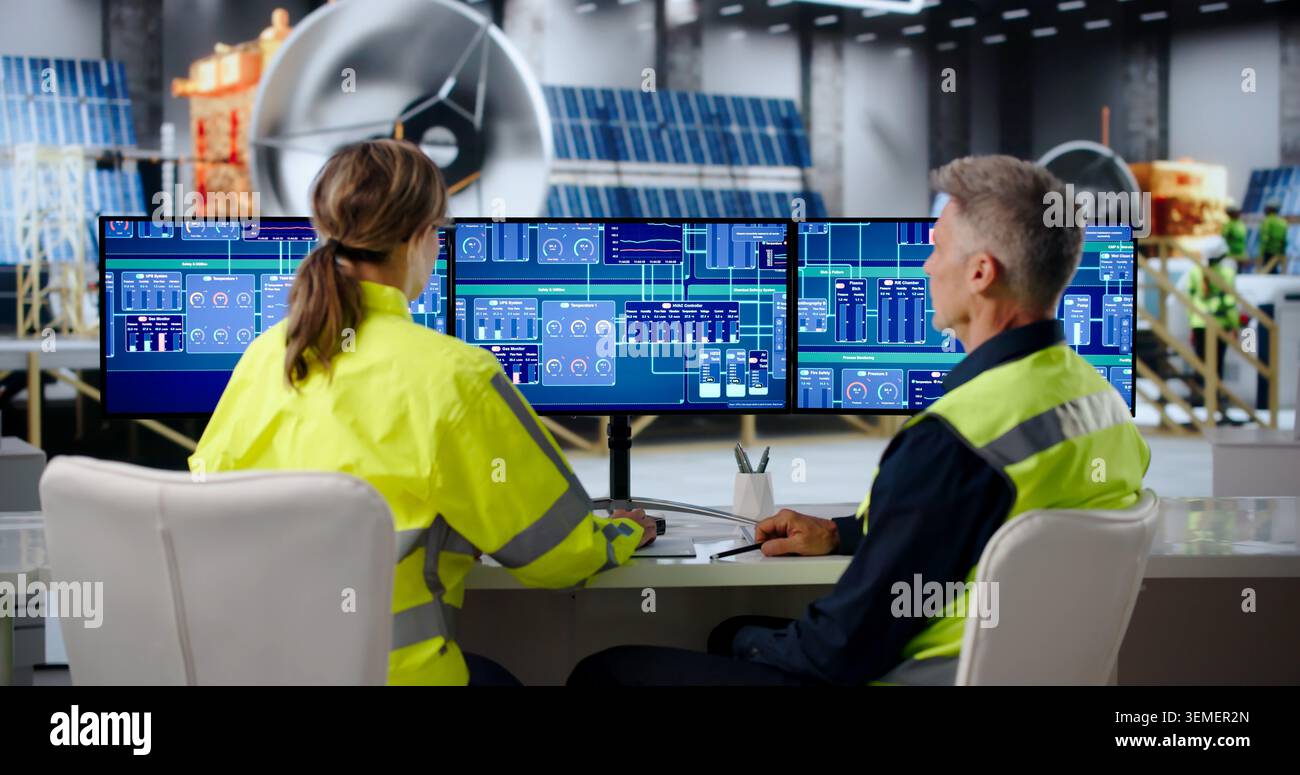 Two Engineers Monitor Satellite Factory Systems Using SCADA Software Together. Stock Photo