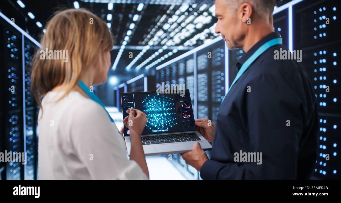 Two Data Scientists Use Laptops Discussing AI Model Development In Tech Center. Stock Photo