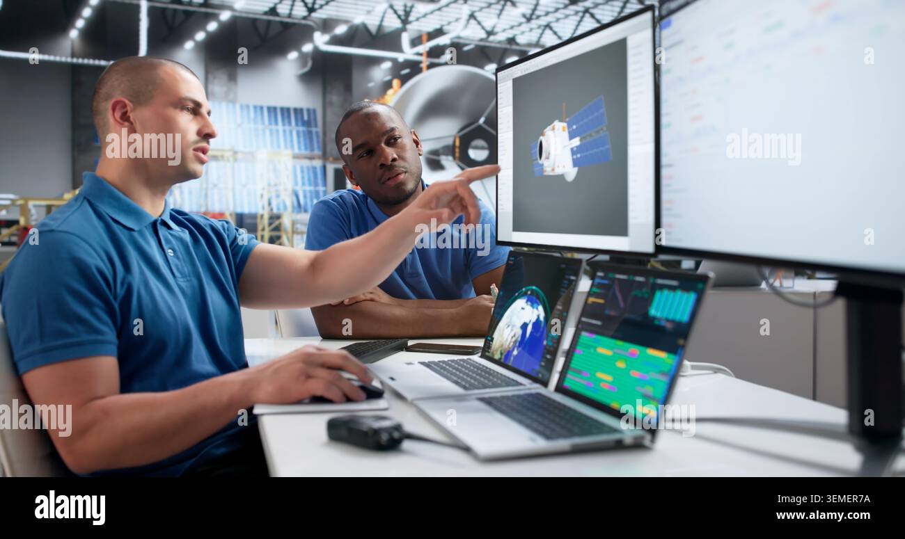 Two Young Engineers Use Computer Software To Design Solar Satellite. Stock Photo