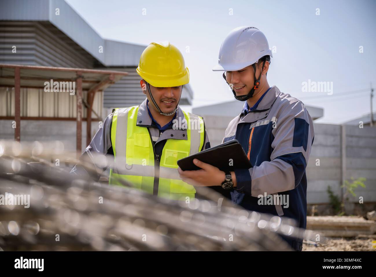 Asian engineer inspecting steel wire mesh construction site, Two builders raw material orders examine in tablet together, They examine coiled steel me Stock Photo