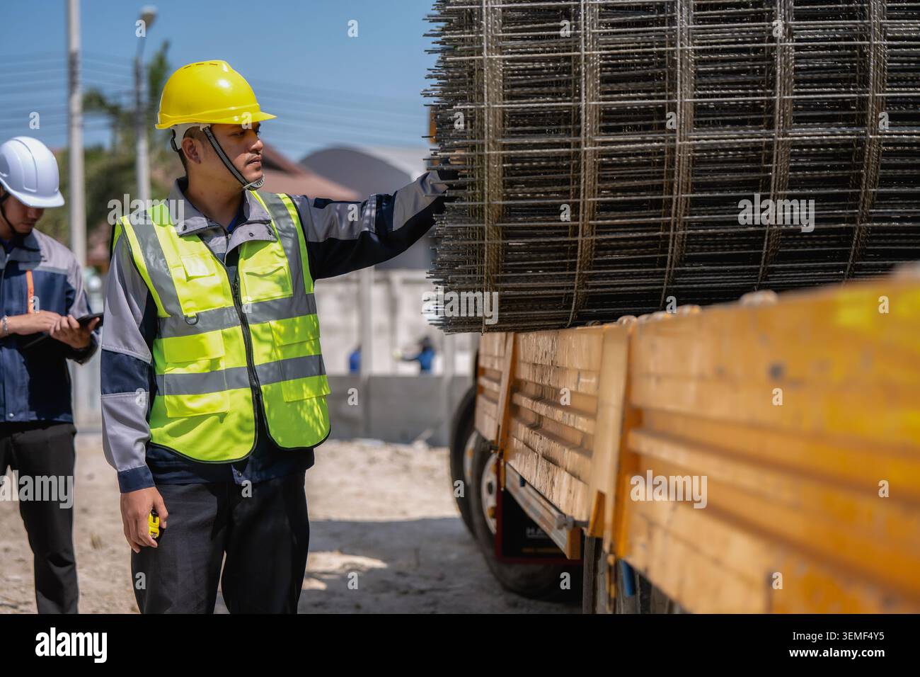 Asian builder inspect the wire mesh on the truck, construction worker in yellow hard hat gestures toward large metal mesh stacked on a truck with civi Stock Photo